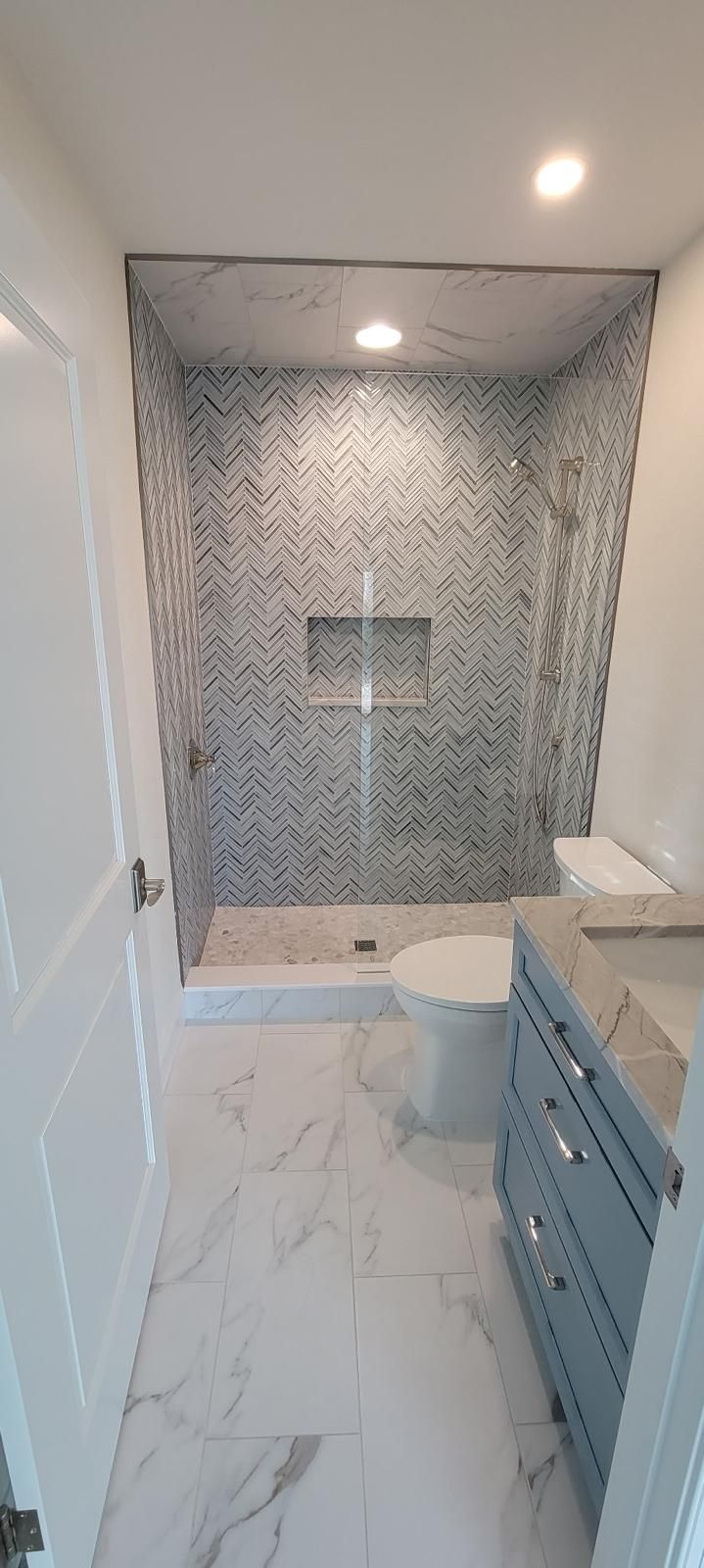 Bathroom remodel with herringbone tile shower and blue vanity